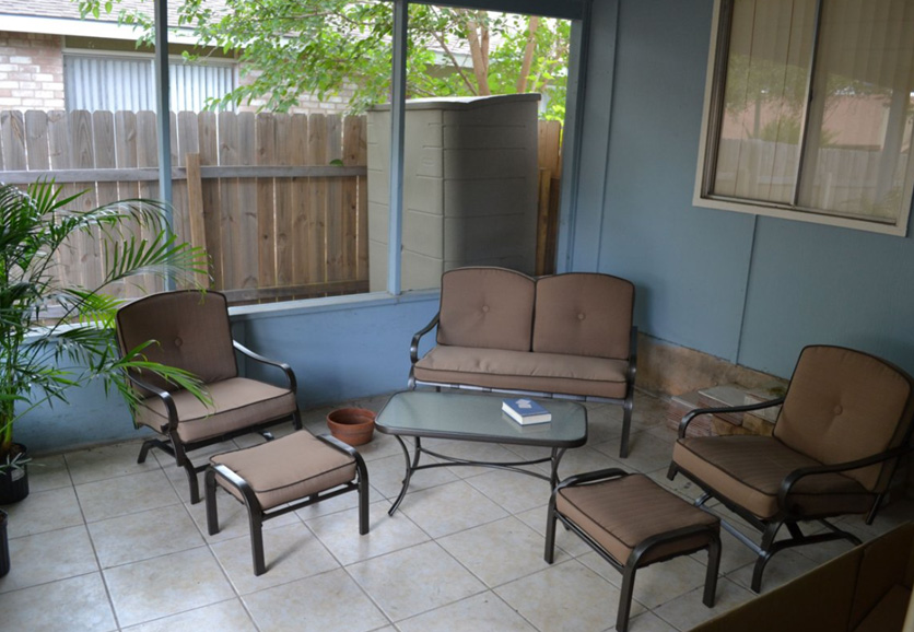 Outdoor patio with wooden chairs and a table set for two, surrounded by lush greenery.